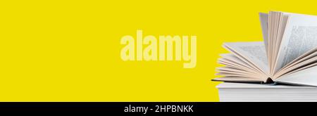 Banner with open book lying at books stack on yellow background. Reading and turning pages. Education and getting knowledge concept. High quality photo Stock Photo