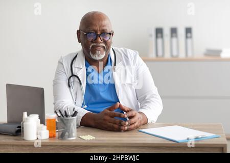 Portrait of smiling doctor looking at camera sitting at desk Stock Photo