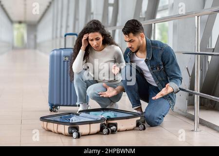 Missed Items. Confused young arab couple sitting near open suitcase in airport Stock Photo