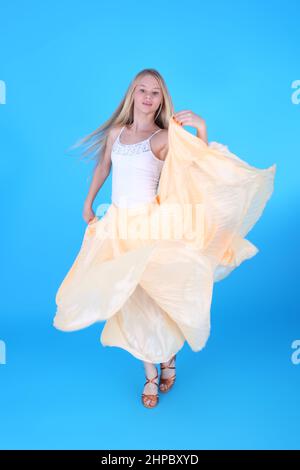 Pretty teenage blond girl dancing in the yellow dress, blue background Stock Photo