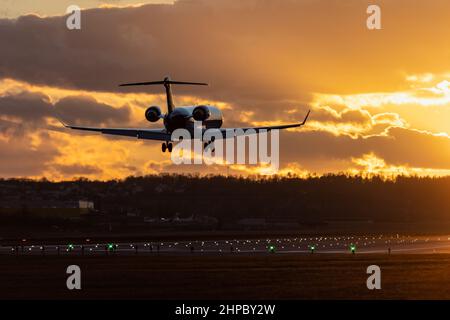 Aircraft landing at Stuttgart Airport, landing gear down, against golden sunset sky with some clouds, partly blurred by heat of jet engines Stock Photo