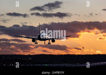 Aircraft landing at Stuttgart Airport, landing gear down, against golden sunset sky with some clouds, partly blurred by heat of jet engines Stock Photo