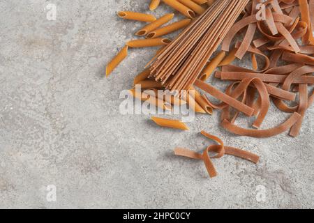 Different types of wholegrain pasta, tagliatelle, and penne rigate, on a rustic gray stone background, healthy noodle alternative, copy space, flat la Stock Photo
