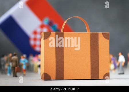 Cardboard suitcase, plastic toy people and a flag on an abstract background, a concept on the theme of moving to Croatia Stock Photo