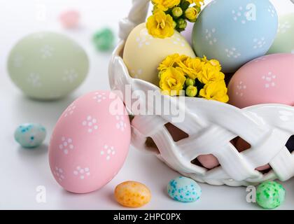 Closeup of colorful easter eggs, flowers and candy in a basket and on a white background Stock Photo