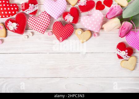 Handmade sewed Valentine fabric hearts with tulips and cookies flat lay background on white wooden table Stock Photo