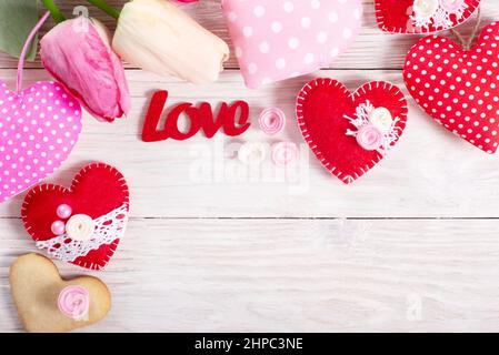 Handmade sewed Valentine fabric hearts with tulips and cookies flat lay background on white wooden table Stock Photo