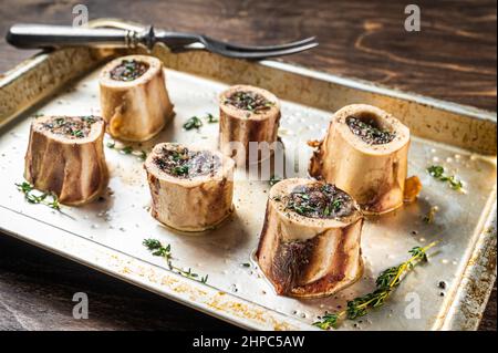 Roasted marrow beef bones in baking dish. Wooden background. Top view Stock Photo