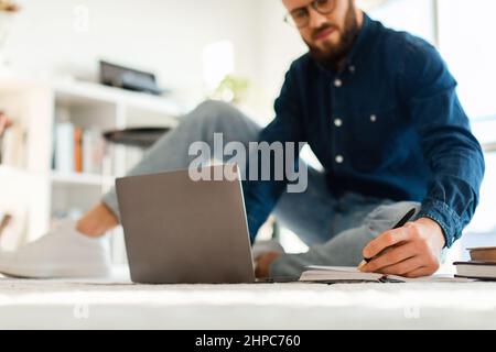 Man Taking Notes Using Laptop Sitting On Floor Indoors, Cropped Stock Photo