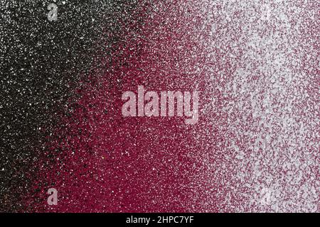 Macro close-up of a painted burgundy red wall with black and white spray paint and splashes. Abstract full frame splattered graffiti background. Stock Photo