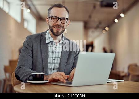Cheerful bearded man using laptop in cafe Stock Photo
