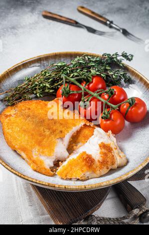 Crispy breaded tilapia filles on a plate with vegetables. White background. Top view Stock Photo