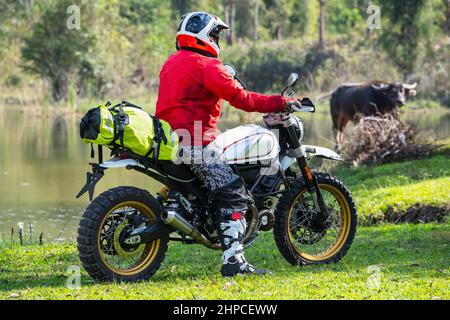 Man with his scrambler type motorcycle on rugged terrain in Thailand Stock Photo