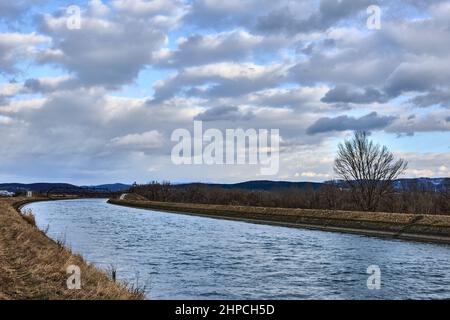 Landscape with waterway and dramatic cloudy sky, gray white clouds. Small ripples on water surface. Natural background, wallpaper.  Trencin, Slovakia. Stock Photo