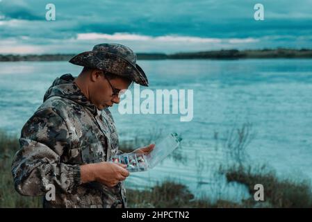 Serious elderly bearded fisherman on river bank holding rod and tackle box  selects fly fishing lure would be better. Copy space. Fly-fishing, active l  Stock Photo - Alamy