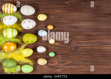 Happy Easter concept. Colorful Easter eggs with bright feathers on a dark wooden background. View from above. Place for inscription, text. Basis for a Stock Photo
