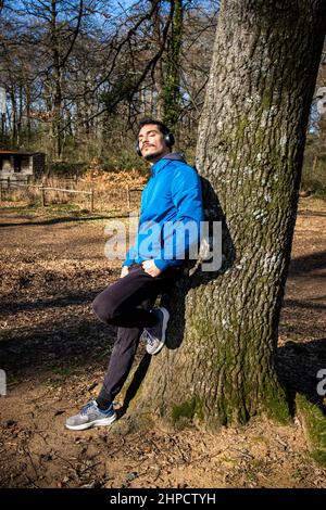 Portrait of a handsome young man with blue eyes and a mustache who is listening to music while exercising. The man in the blue jacket is training in t Stock Photo