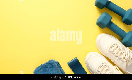 Blue dumbbells, towel, fitness tape and feminine sport shoes isolated on yellow background. Fitness or workout items, top view. Sport blog wide banner Stock Photo