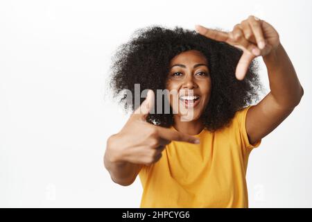 Creative black woman looking through hand frames gesture and smiling, picturing moment, taking picture of moment, measuring something, white Stock Photo