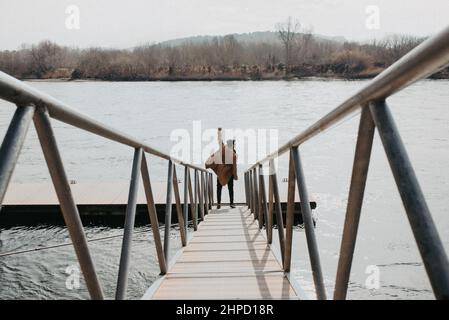 Man at the end of a wooden footbridge next to a river raising an arm in victory. Success and self confidence Stock Photo