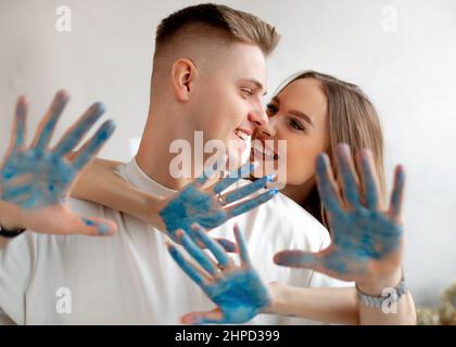 Happy smiling young amazing woman stand behind man in white T-shirts, meeting eyes showing hands covered with blue paint Stock Photo