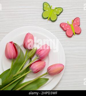 Spring holiday table setting. Fresh pink tulip flower decoration on white plate, white wood background, top view Stock Photo