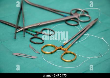 Sterilized surgical instrument on green fabric background. Surgeon doctor stainless steel tool, forceps, needle holder or driver, scissor, blade, sutu Stock Photo