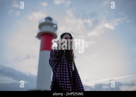 Woman dropping a handful of sand in front of her face. Vacation by the sea and a lighthouse. Stock Photo