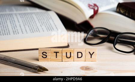 Word STUDY written with wooden blocks, along with pens, glasses and books on a table. Study and knowledge concept Stock Photo