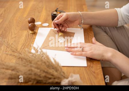 Cropped photo woman hands making stamp certificate present envelope craft, sit wood desk, putting sealing wax print.  Stock Photo