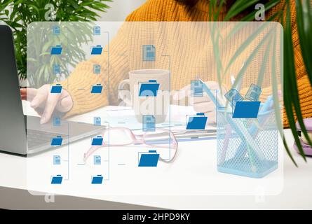 a woman sits at a white table and works at a laptop. Screen with file structure, archiving and organizing documents. Document management system Stock Photo