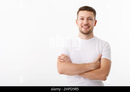 Portrait of a cheerful young man in a white T-shirt on a white background. The guy is standing looking at the camera and smiling. Stock Photo