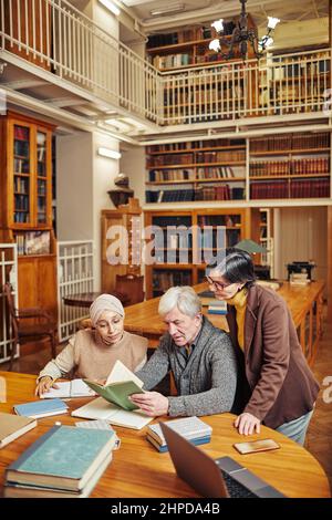 Vertical portrait of white haired senior man studying in library with diverse group of students, copy space Stock Photo