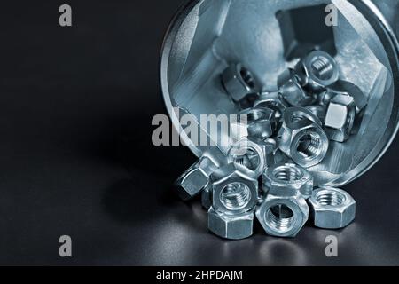 Small hex nuts spilled on heap in big socket for ratchet wrench with reflection on a black background. Close-up of stainless steel hexagonal fasteners. Stock Photo