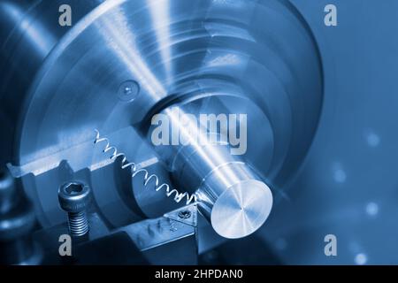 Lathe tool bit and spiral swarf at working on a metal product. Close-up of steel knife with carbide insert and turning machine. Blue toned background.