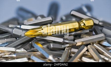 Big golden cross screwdriver bit on silvery bits heap of various size and type. Closeup of metal slot or cruciform screw drives with hex shank on pile. Stock Photo