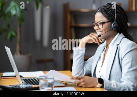Young positive afro female using wireless headset for remote work during maternity leave Stock Photo