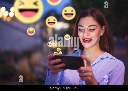 Young Caucasian redhead woman laughing into smartphone at night in city Stock Photo