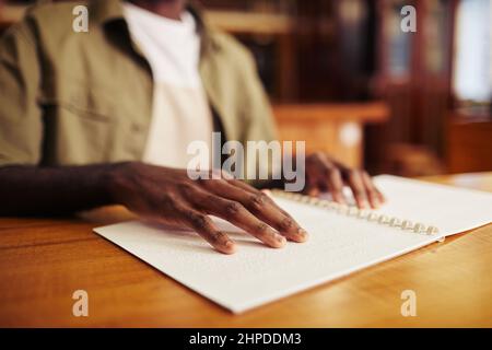 Close up of young black man with vision impairment reading book in braille at table in college library Stock Photo