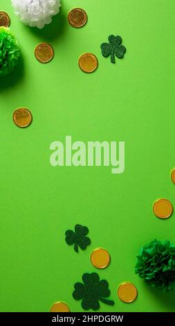 Irish Saint Patricks day concept. Vertical banner mockup with gold coins, clover leaves, decorations on green background. Flat lay, top view, copy spa Stock Photo