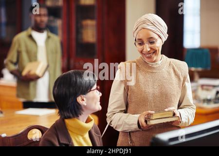 Warm toned portrait of smiling young woman talking to female librarian in college library Stock Photo