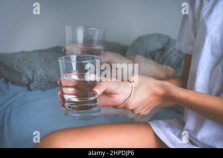 Woman holding glass of water in shaky hands and suffering from Parkinson's disease symptoms or essential tremor. Stock Photo