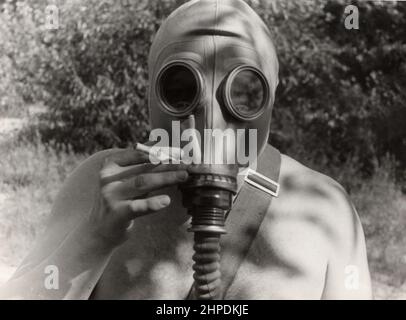 Trekhizbenka village, Lugansk region, USSR - circa 1982: Vintage photo of a soldier in a gas mask without clothes. Humor. The man is holding a cigaret Stock Photo