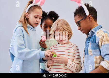 Diverse group of children wearing bunny ears and playing with Easter eggs against white background Stock Photo