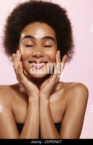 Vertical shot of african american woman model, applying toner, face lotion and smiling, smooth and fresh skin. Attractive young black female with Stock Photo