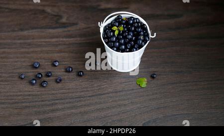 Heap of American blueberries scattered from a white bucket, on a black wooden background Stock Photo