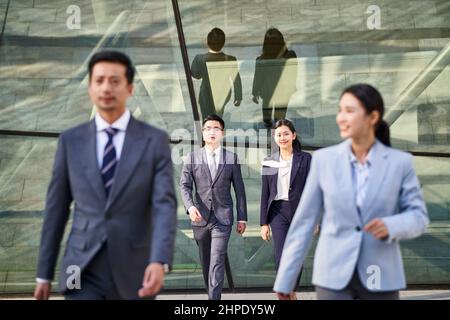 four young asian business people men and women walking outdoors, focus on background Stock Photo