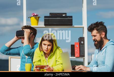 Modern technology. Young men and women sitting at a table with virtual reality goggles. Business team testing virtual reality headset in outdoor Stock Photo