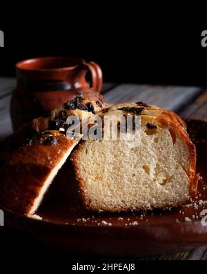 A clay or mud Mexican hand made plate, with sweet bread and raisins on top and a steaming cup of coffee or hot chocolate cocoa in the background. Stock Photo