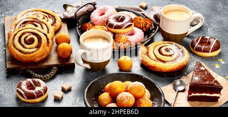 Table with various cookies, donuts, cakes and coffe cups on dark backround. Panorama Stock Photo